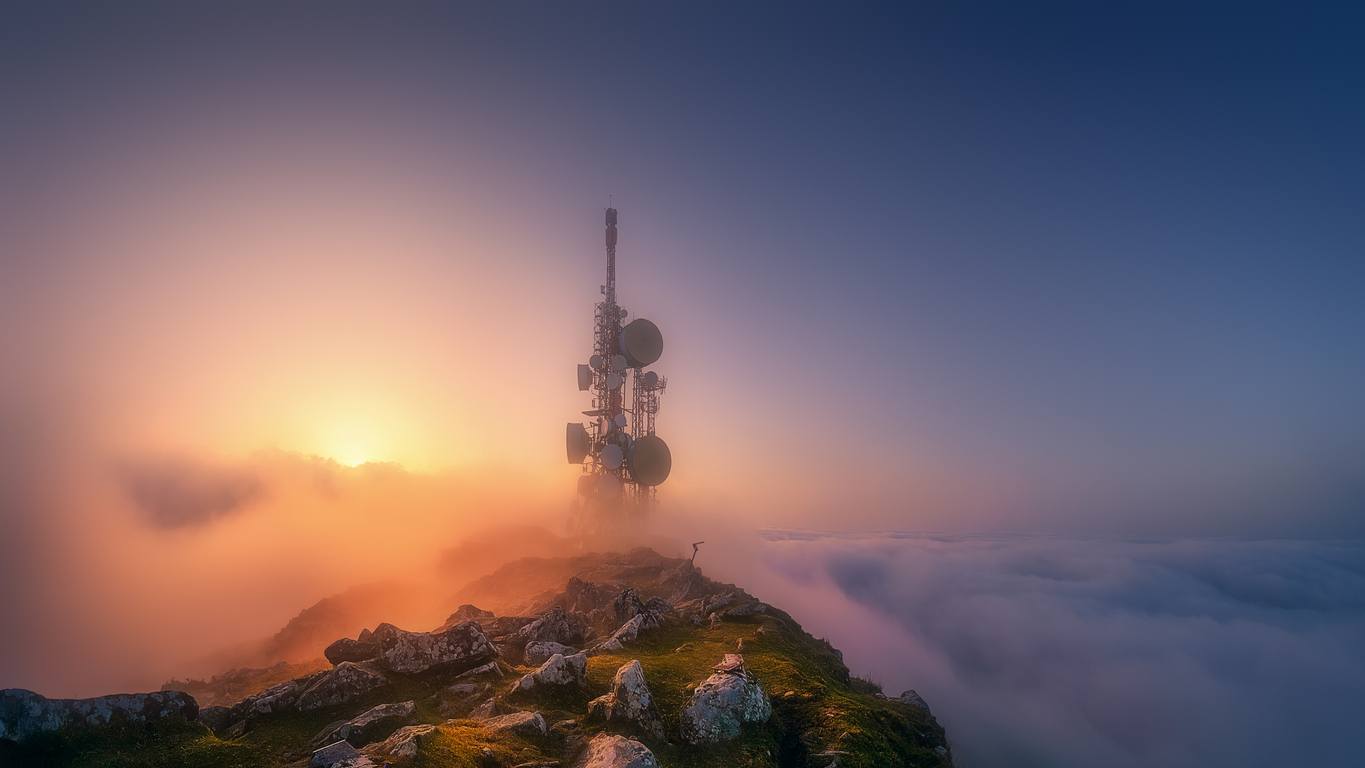 5G communications and telecommunications tower on mountain top at sunset.